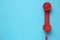 Red corded telephone handset on light blue background, top view. Hotline concept