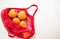 A red cotton string bag with persimmons and tangerines lies on a white background. The concept of saving the earth from plastic.