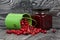 Red cranberries in an overturned green bucket. Lies on brushed boards. Next to it is cranberry jam in a jar