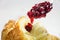 red cranberry jam on a spoon dripping on a fresh croissant, breackfast closeup