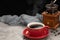 Red cup of black coffee with smoke, grinder and coffee beans on cement table