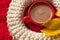 A red cup of cocoa, a beige knitted scarf and yellow autumn leaves placed n a red surface
