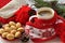 A red cup of hot coffee, a red and white knitted scarf with pompons, a fir twig, cones and Christmas-tree decorations