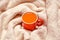 Red cup of hot sea buckthorn tea on backdrop from white knitted sweater on a rustic wooden background. Immunization concept. Flat