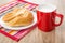 Red cup with milk, napkin and bun in white plate