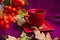 Red cup with tea on saucer on purple knitted background with autumn leaves and rowan berries