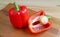 Red cut bell pepper and whole bell pepper with water droplets on a wooden cutting board