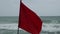 Red danger flag weaving on windy sea beach