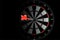 Red dart arrow hit in the target center of dartboard on black background