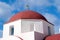 Red dome with cross detail in Mykonos, Greece. Church building architecture on sunny outdoor. Chapel on blue sky