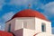 Red dome with cross detail in Mykonos, Greece. Church building architecture on sunny outdoor. Chapel on blue sky