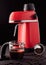 Red domestic coffee machine with a filled glass jug and a portafilter, decorated with ground and whole grains