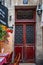 Red door with ornate metal gratings. Ancient architecture of Paris France. Antique building near French cafe with chairs on street