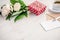 Red dotted gift box, kraft envelope and empty greeting card, coffee cup and peony flowers bouquet over white wood background. Copy