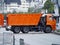 A red dump truck stands across the road, blocking it. Urban background with truck