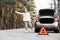 Red emergency triangle with blurred car and woman calling car mechanic in the background. Accident and broken car on the