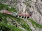 Red express train on scenic stony St. Gotthard railway bridge and tunnel, swiss Alps, SWITZERLAND