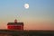 Red farm shed with cupola atop a hill with bright full moonrise above