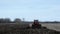 Red farm tractor pulling cultivator turning up black soil on field after harvest of soy beans.