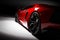 Red fast sports car in spotlight, black background. Shiny, new, luxurious.