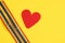 red felt heart and two bracelets with lgbt colors on yellow background copy space top view, pride concept