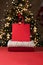 Red festive sparkling shopping bag mockup, sweaters stack on red table, blurred shiny Christmas tree background