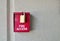 Red fire access box with padlock on a plain textured wall.