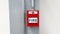 Red fire alarm button for pull out in emergency case happen in stalled on gray or grey steel pole with white wall background