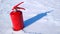 Red fire extinguisher on a winter surface of white shiny snow with a shadow from snow drifts