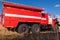 Red firetruck car Ural rides through the autumn field with yellow and faded grass against the blue sky and clouds. The concept