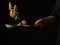 Red fish with herbs in a frying pan held by the hand of the cook. Black frying pan, black background. Focusing on the foreground.