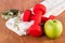 Red fitness dumbbell, measuring tape and green fresh apple with dew on white towel and wooden floor