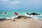 Red flag standing on the rocky coast of the Gulf of Thailand against the backdrop of the blue sea. Hazard warning during storm