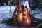 Red flames of teepee campfire on snowy ground at campsite in wild at dusk, closeup bonfire, winter camping at night