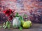 Red flower with green leaves  in  small vase  , green apples   on wooden table .Copy space