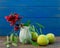 Red flower with green leaves  in  small vase  , green apples   on wooden table .Copy space