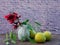 Red flower with green leaves  in  small vase  , green apples   on wooden table .Copy space