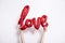 Red foil Love balloon held against a plain white background