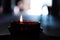 Red glass burning candle close-up in dark interior with light on background