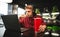 Red glass with a cool drink on the background of a young man who works on a laptop in a cafe and eats fast food. Freelancer works