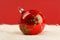 Red glossy christmas ball with green stars on white fur in front of red background