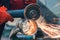 A red-gloved mechanic cleans a welded seam on a section of a steel pipe with the help of a grinding machine in the metal workshop