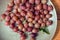 Red gooseberry berries in a clay plate on a wooden background. Collected in the summer from a gooseberry bush.