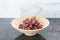 Red grape twigs in a wooden bowl on a granite table over light g