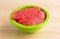 Red grapefruit sections in a green bowl on a wood table