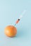 A red grapefruit on which stands a syringe that has extracted fresh juice on a blue background. Fruit Summer vitamin concept.