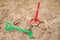 Red and green kids toddlers plastic play shovels laying on a sandbox sand background