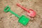 Red and green kids toddlers plastic play shovels laying on a sandbox sand background