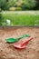 Red and green kids toddlers plastic play shovels laying on a sandbox sand background