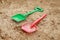 Red and green kids toddlers plastic play shovels laying on a sandbox sand background